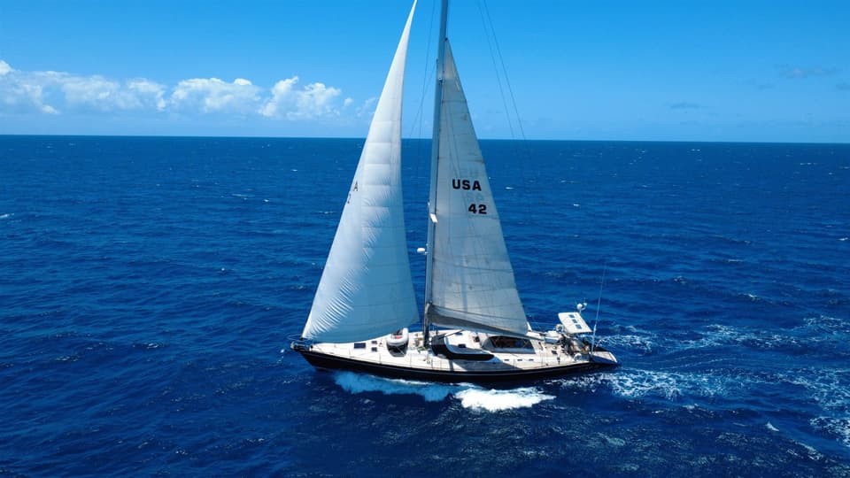 El Cap II, velero de casco azul marino con número de vela USA 42, a toda vela en agua tropical azul.